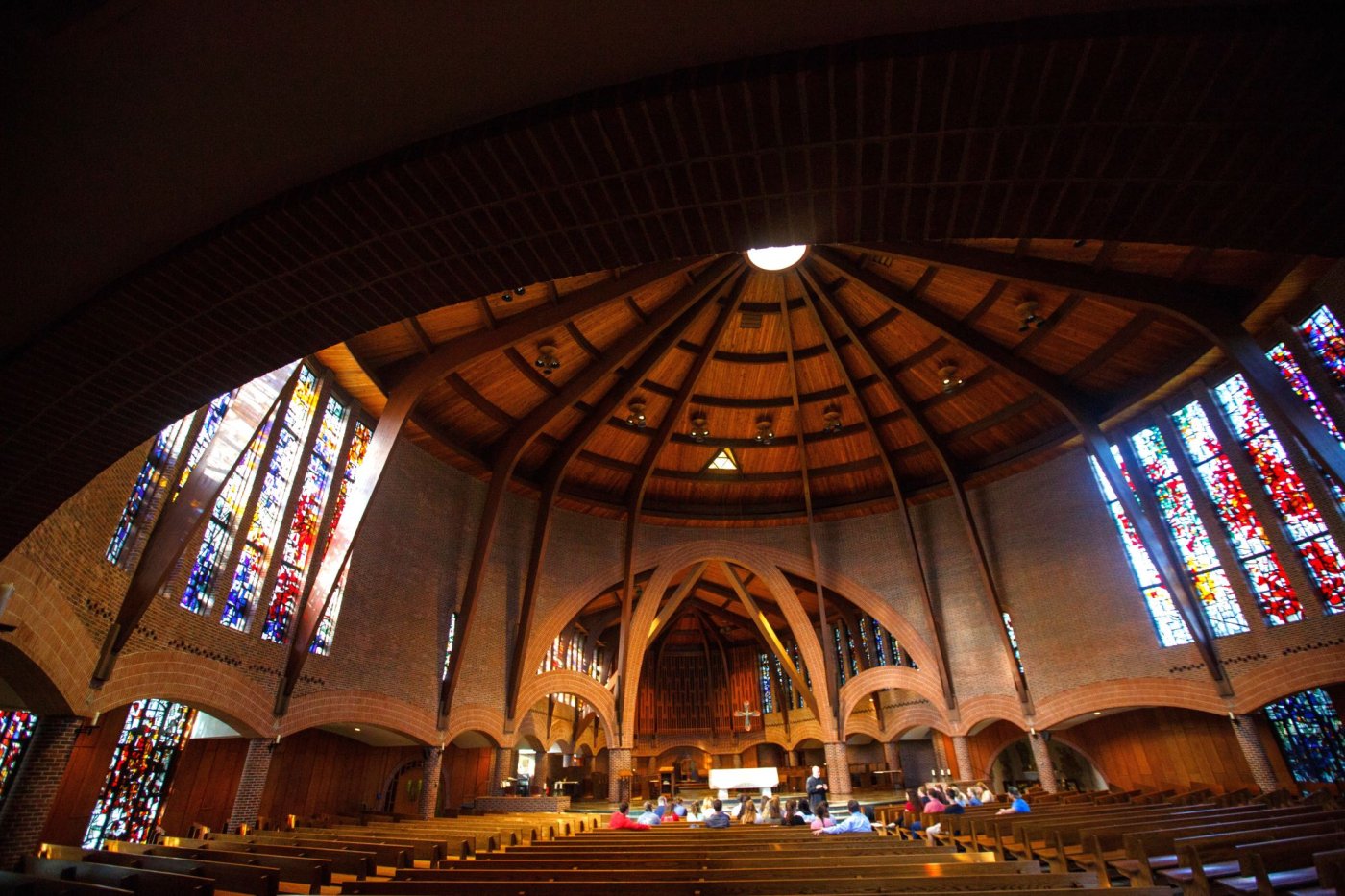 Photo of Abbey Church interior showing vaulted timber roof of cylindrical space, stained glass windows on the walls to either side, and brick arches