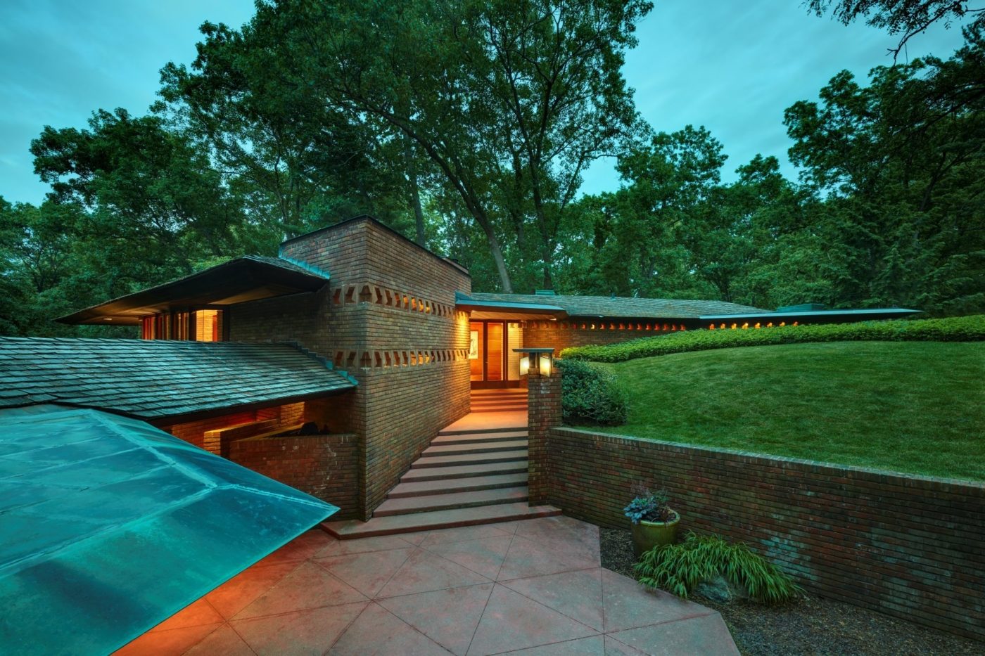 Exterior of Palmer House at dusk showing horizontal roof, massive brick walls with light coming through openings, and stairs up to an entrance