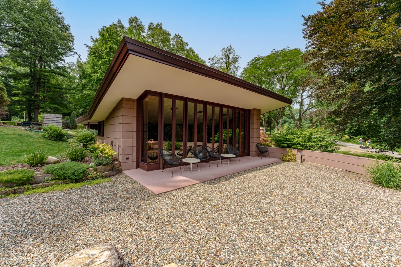 Exterior of Eppstein house with gravel in foreground, concrete patio under cantilevered overhanding roof, wall of glass doors beyond