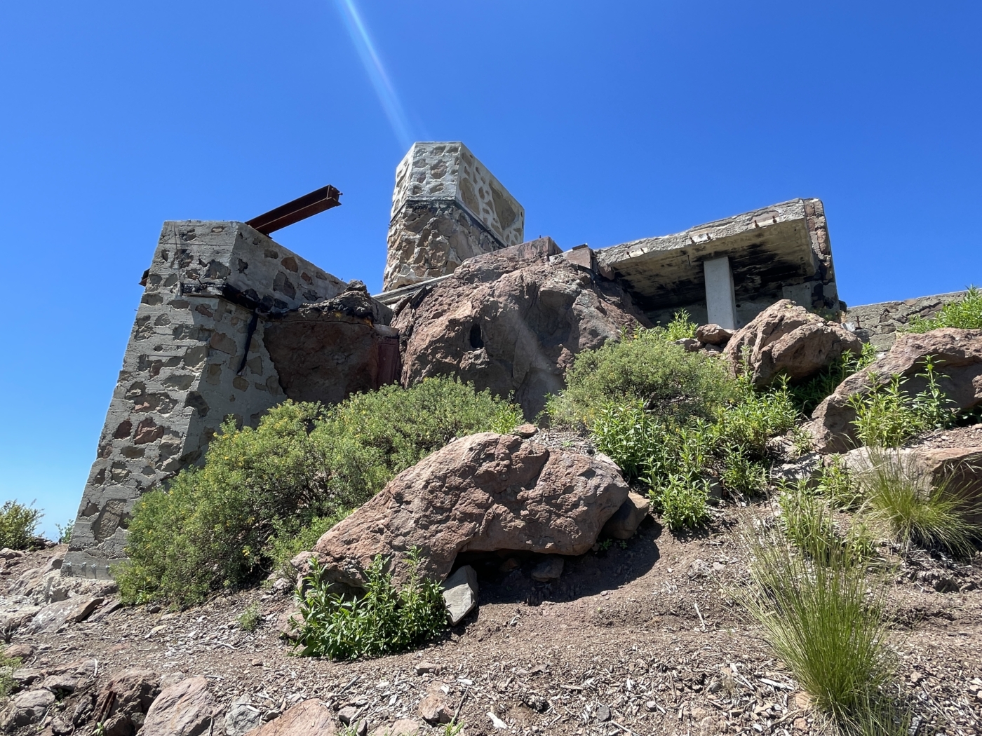 Looking up a scrubby hillside towards rocks and remnant of a desert masonry structure