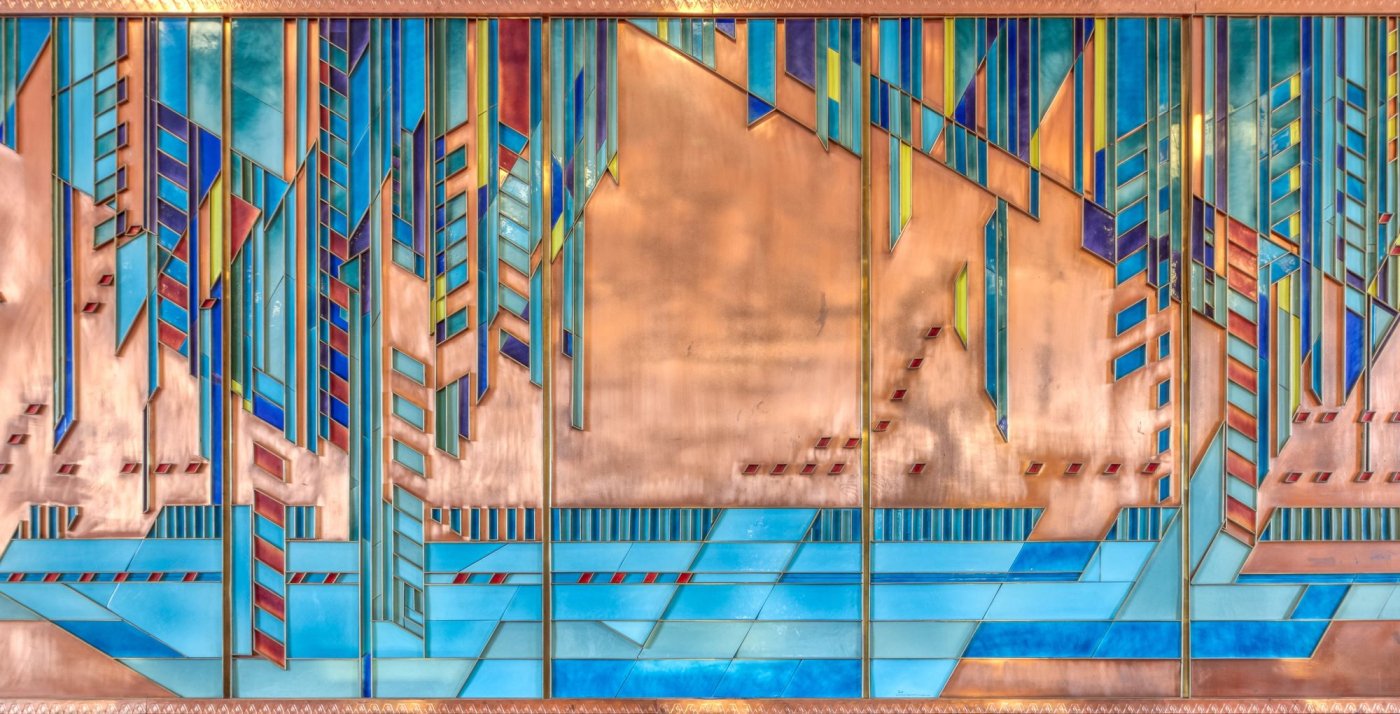 Detail of wall inside Price Tower showing copper-colored backdrop with brightly-colored geometric shapes overlaid in blue and other bold hues, as designed by Frank Lloyd Wright