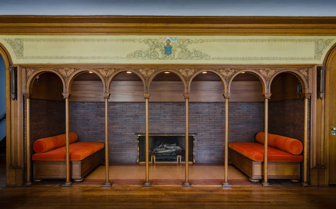 View showing brick fireplace inside Winslow House with wooden arches in front of it, and an intricate painted frieze above