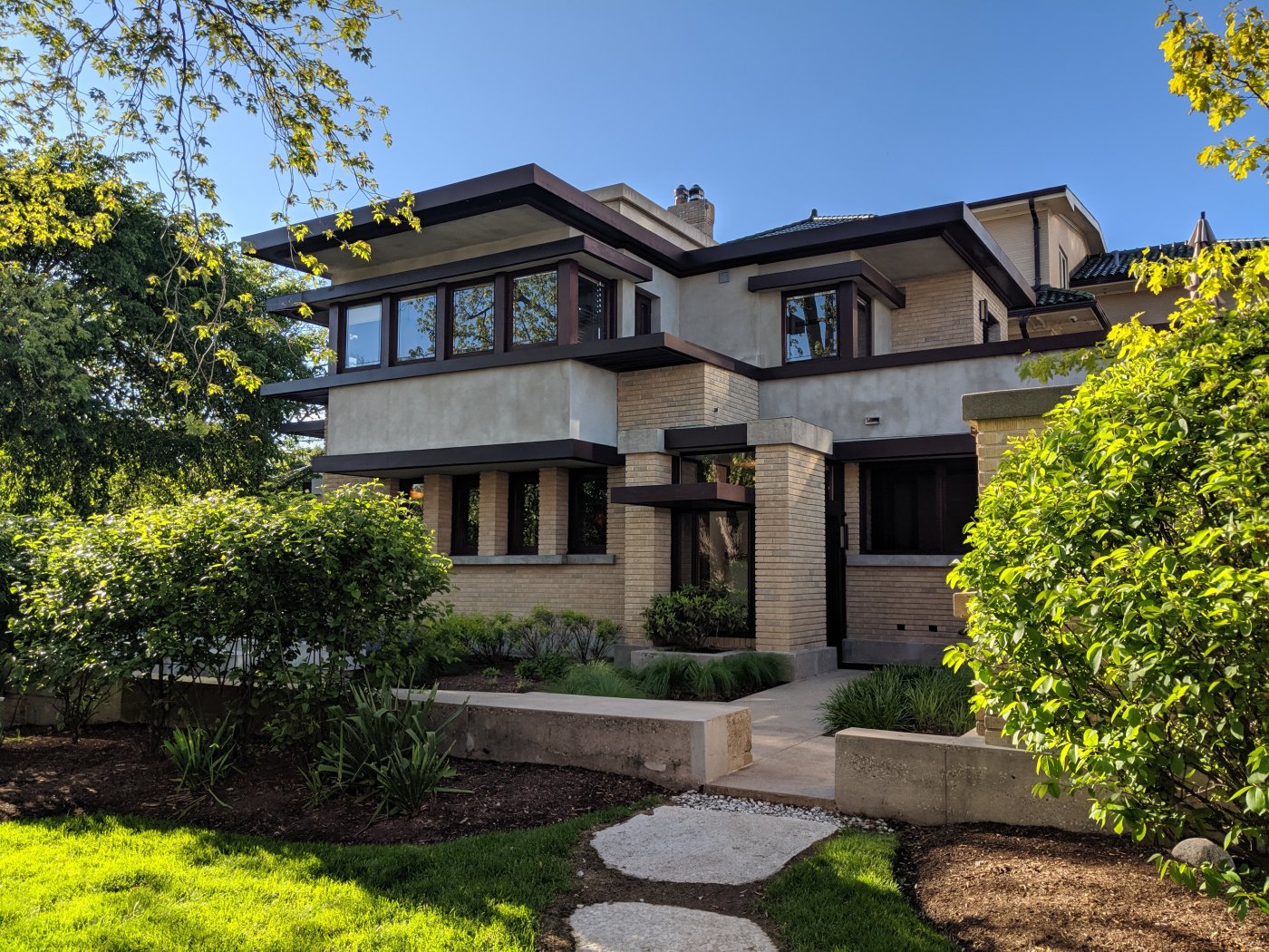 Photo of exterior of Emil Bach House, a Prairie period houses with tan brick and stucco walls, wood trim, flat roof, and bands of square windows.