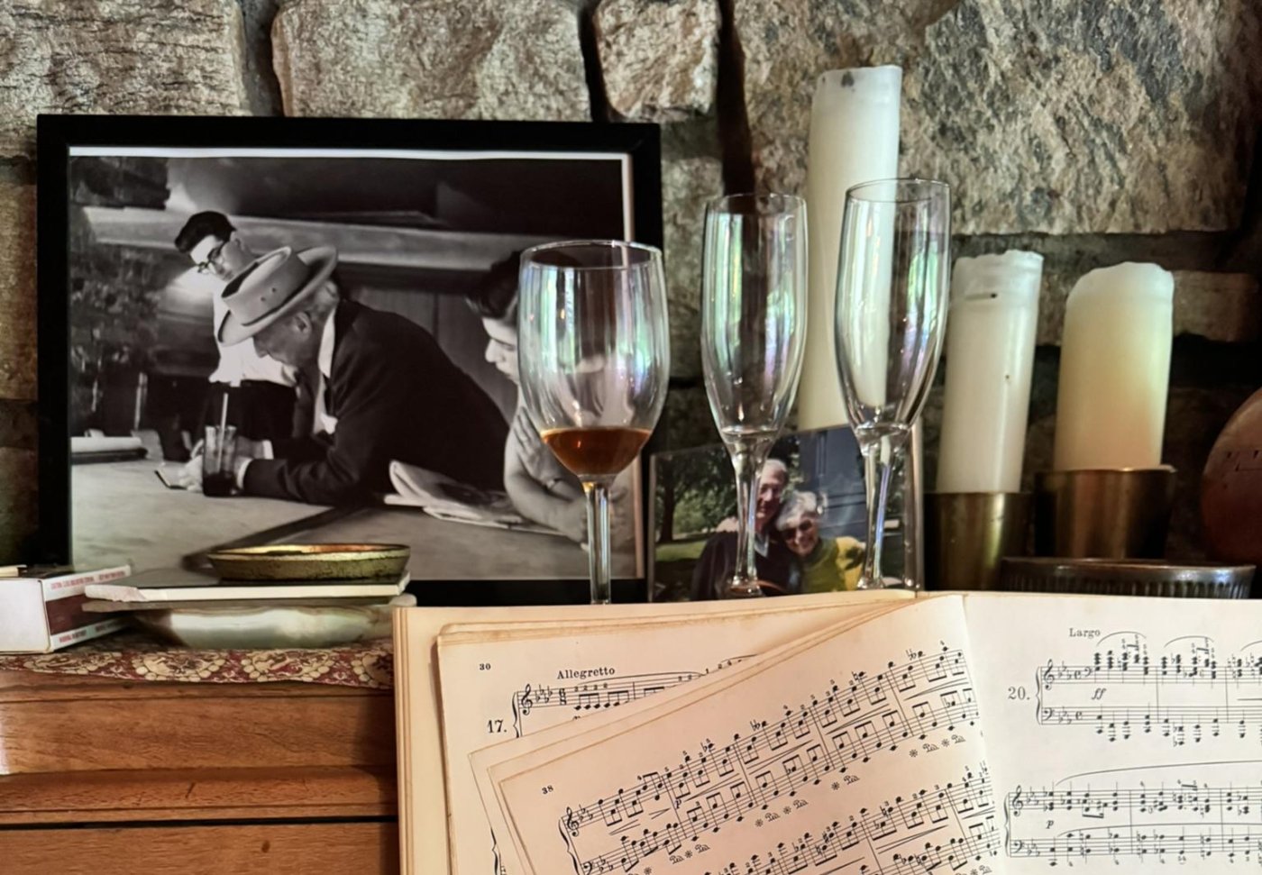 Sheet music, champagne flutes, and a framed photo of Frank Lloyd Wright with a young Roland Reisley on top of a wood piano, against a stone wall.